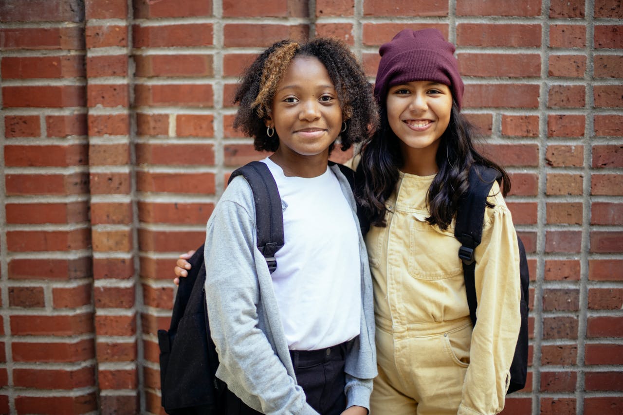 Two diverse teenagers happily posing with backpacks outdoors.